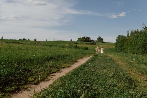 Free A couple leisurely walking on a rural path surrounded by lush fields and trees on a sunny summer day. Stock Photo