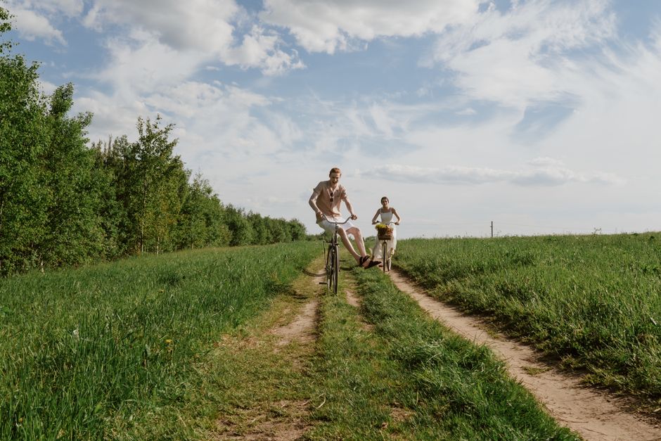 A couple cycling on a grassy rural path under a bright sky, enjoying the outdoors.