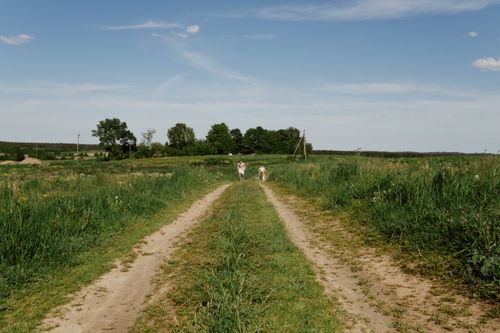 Free Peaceful rural scene with two people strolling a dirt road under a bright blue sky. Stock Photo