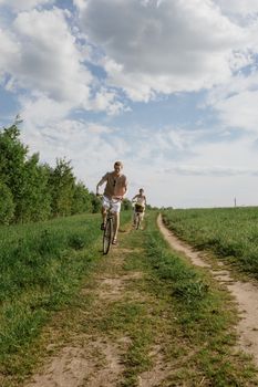 A couple enjoying a leisurely bicycle ride on a rural dirt road surrounded by fields and trees.