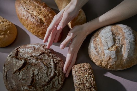 Hands gently touching various homemade breads in a warm-lit, artistic food photography shot.