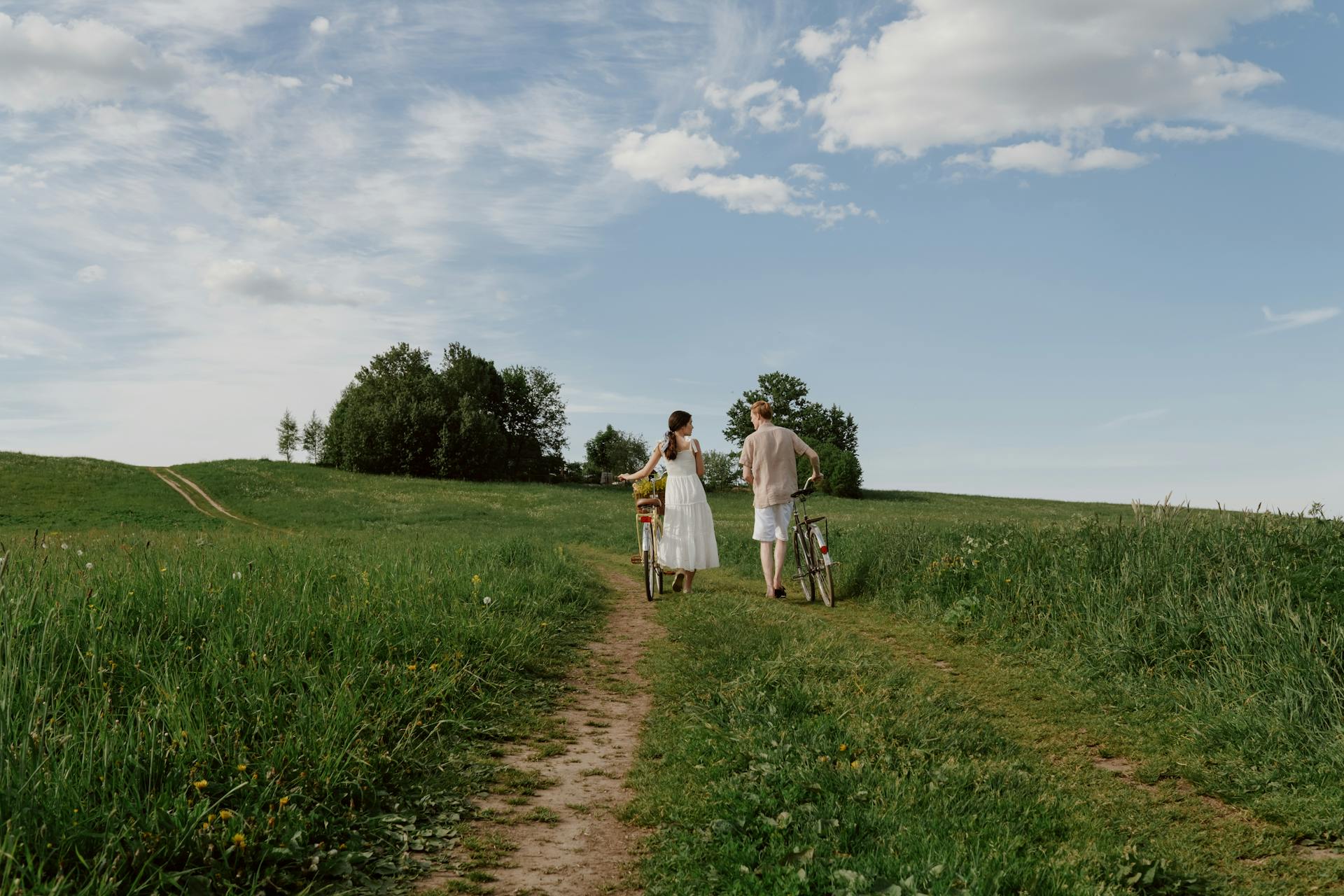A couple walking with bicycles through a scenic rural landscape on a sunny day.