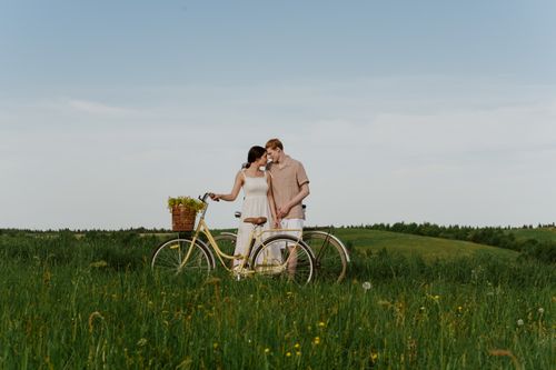Free Loving couple with a bike in a grassy summer field, enjoying nature outdoors. Stock Photo