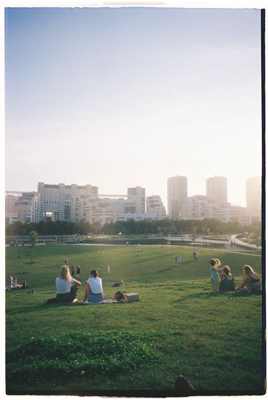 People sitting on a park lawn with a city skyline at golden hour — photo by Диана Дунаева on Pexels