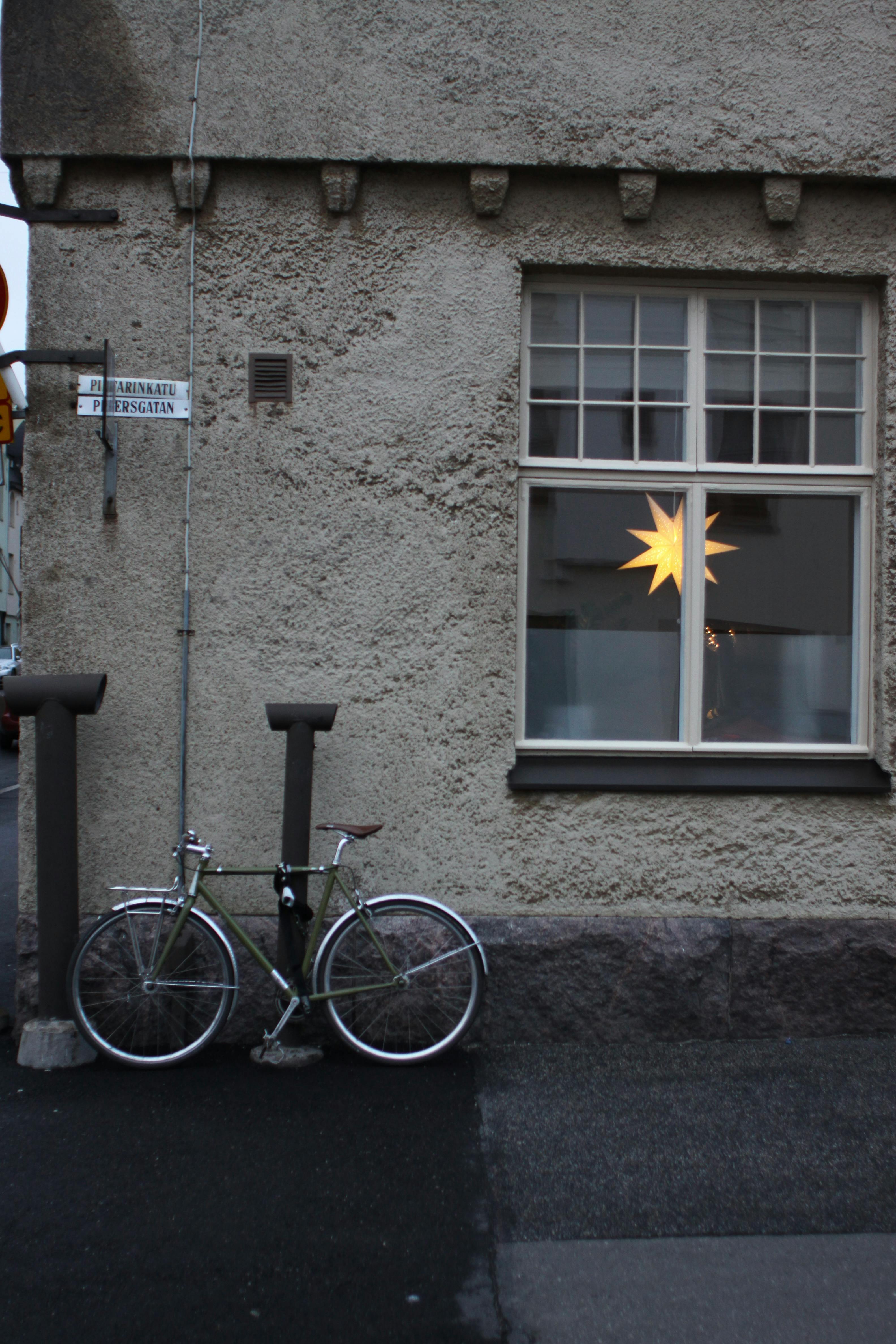 Bicycle parked by building with window light in a quiet street corner.