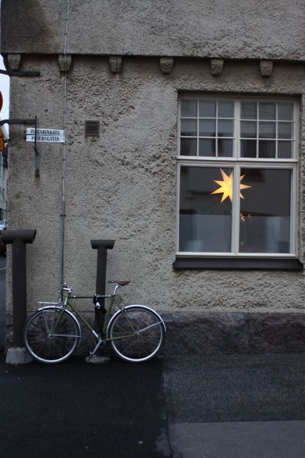 Bicycle parked by building with window light in a quiet street corner.