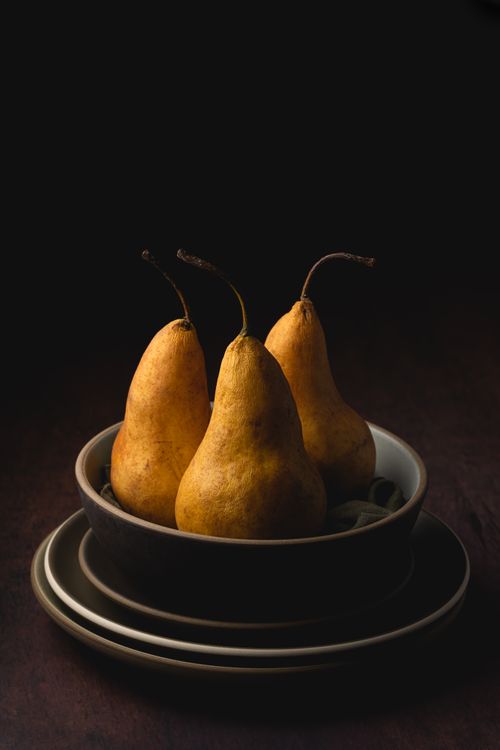 Free Artistic still life of three yellow pears in ceramic bowls against a dark background. Stock Photo