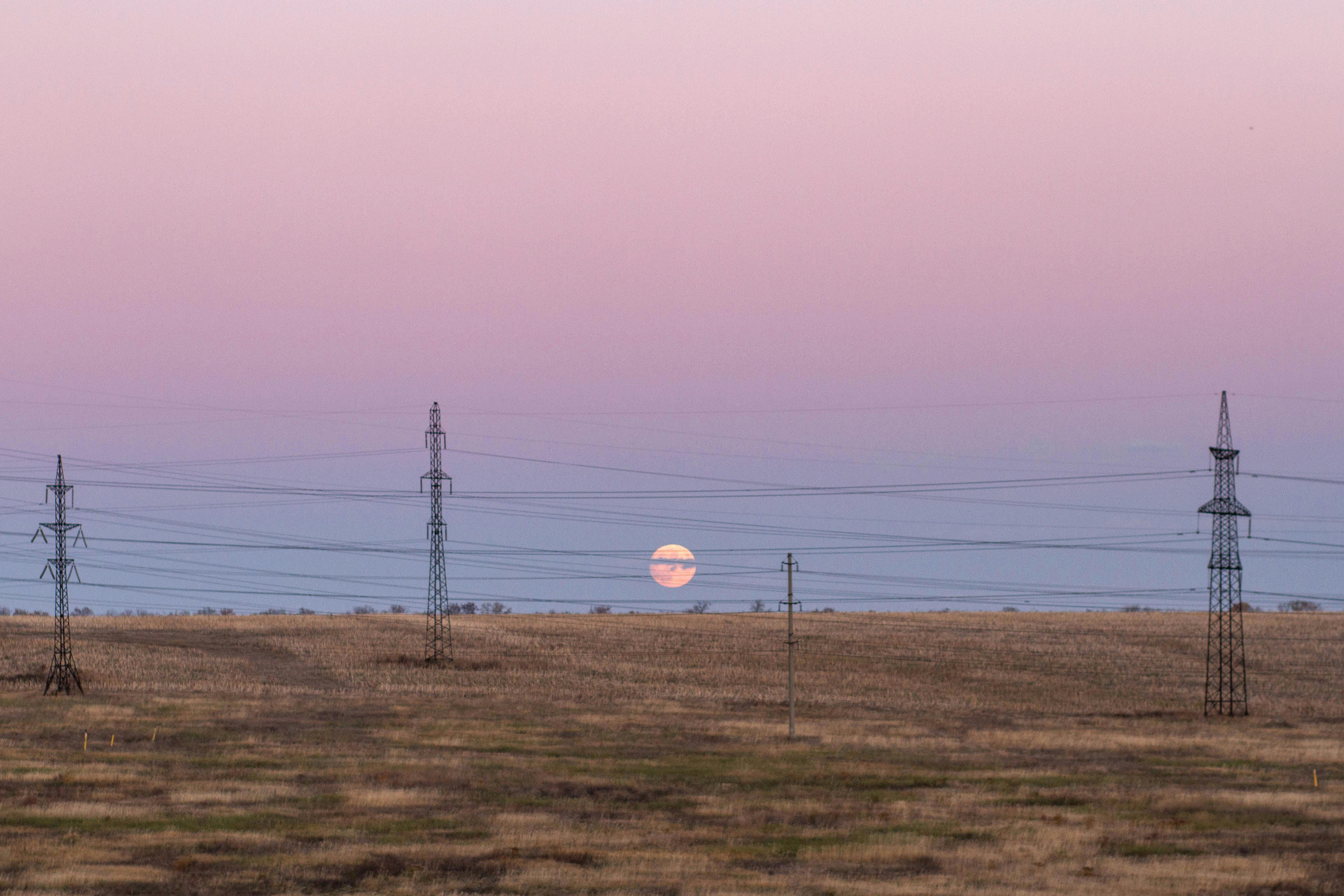 Serene twilight scene with the moon rising over power lines in an open field.