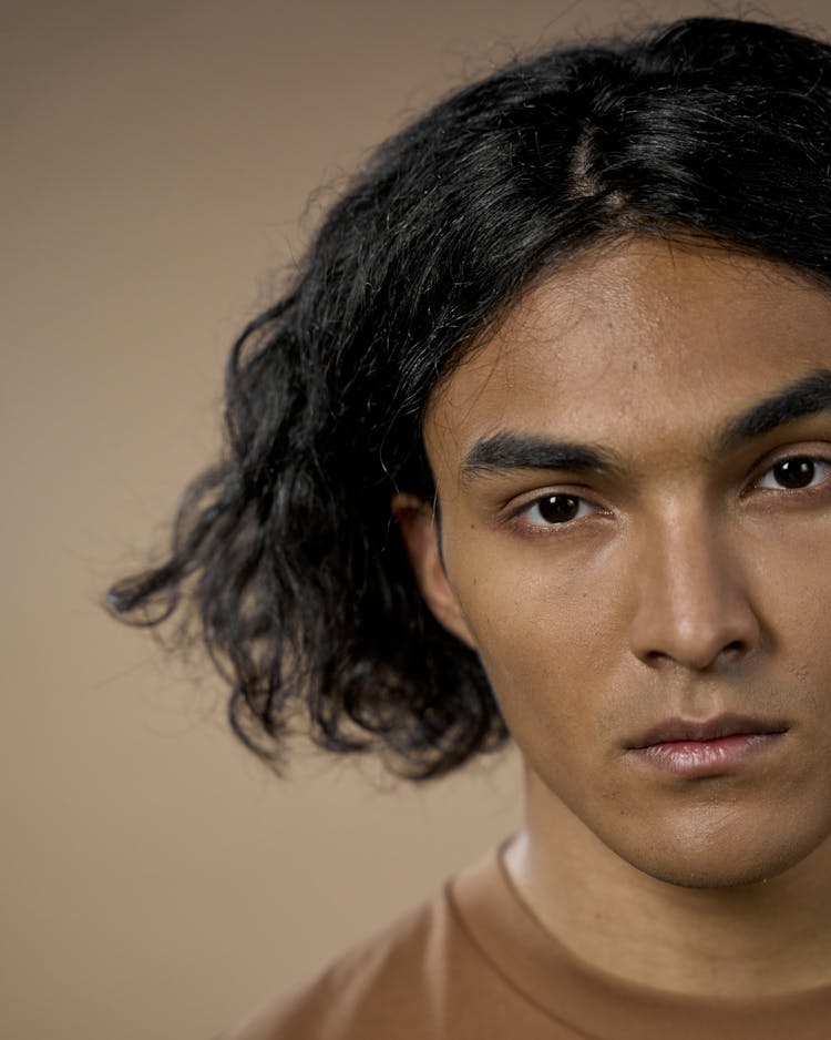 A Man In Brown Crew Neck Shirt With Wavy Hair
