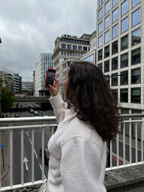 Free A woman in a white sweater takes a photo with her smartphone on a city bridge, showcasing modern architecture. Stock Photo
