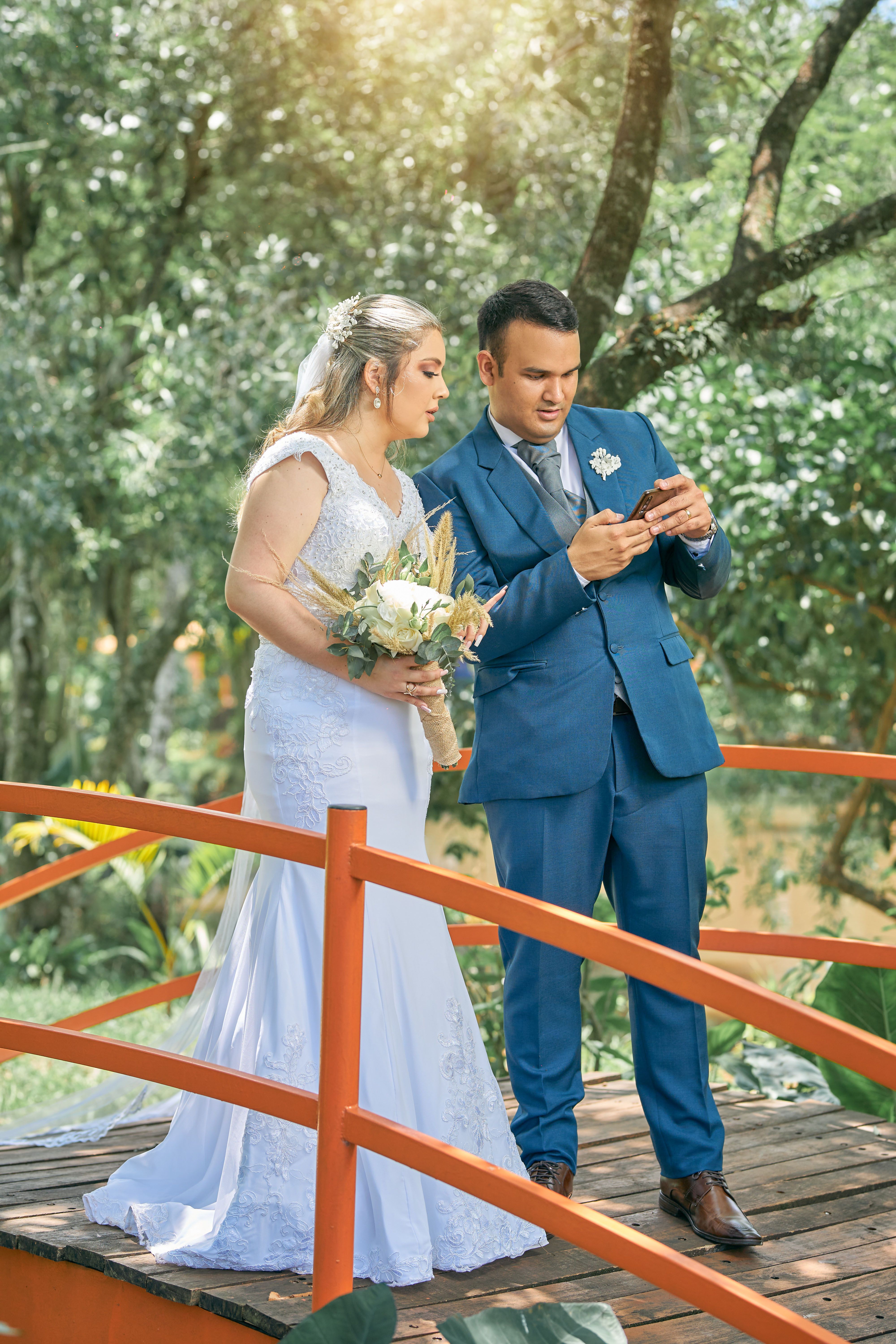 Couple in wedding attire standing on a wooden bridge, celebrating their marriage outdoors.