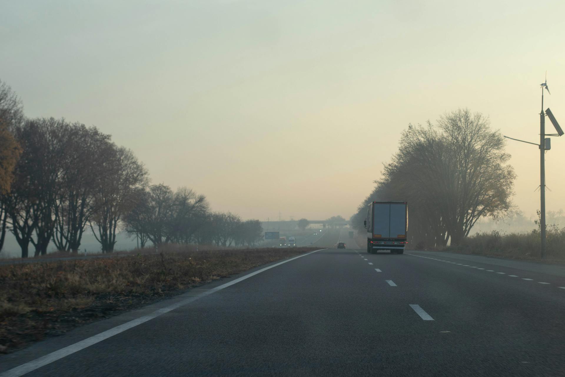 Peaceful morning highway scene with a truck driving surrounded by misty trees.