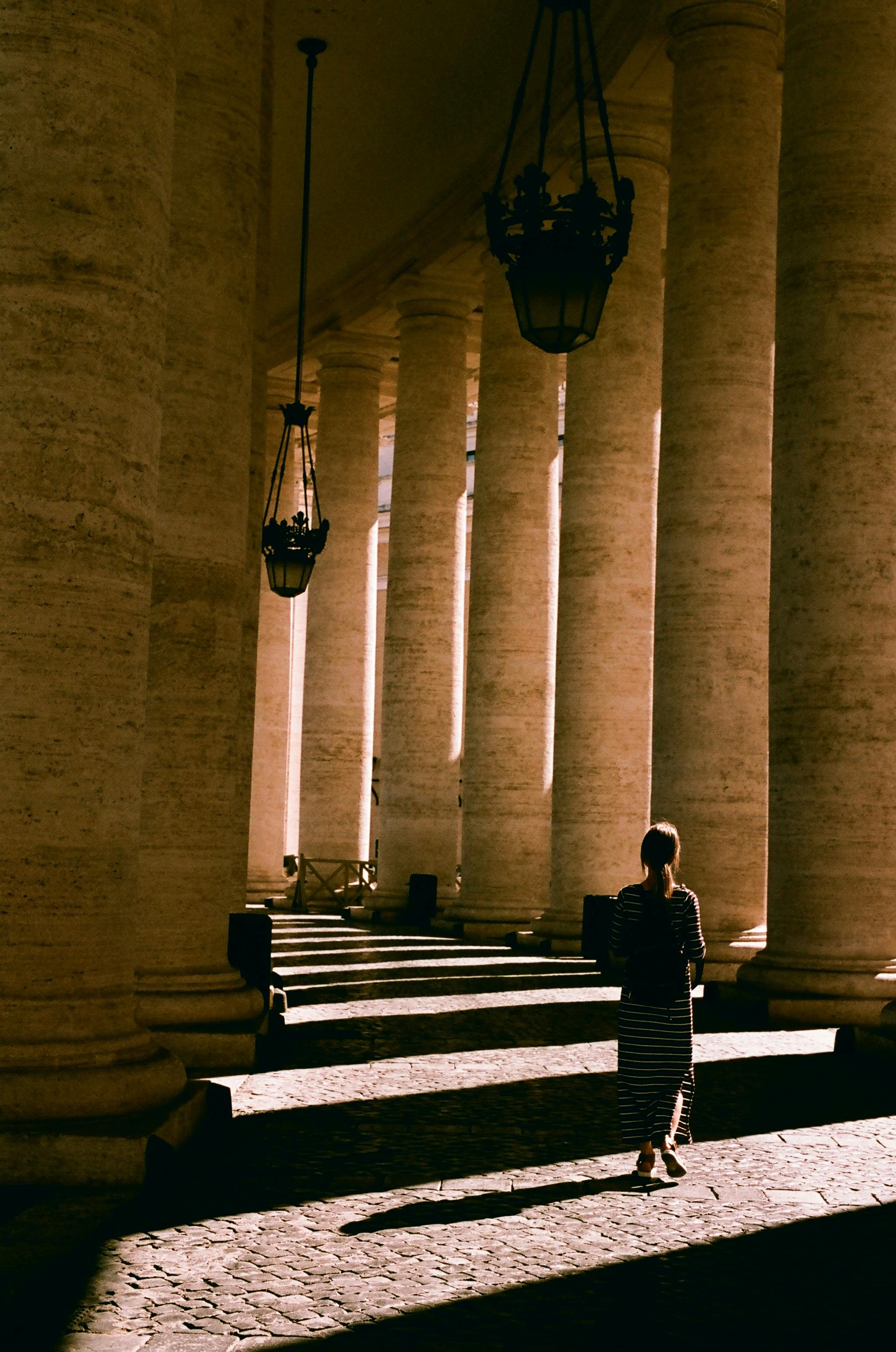 Silhouette of a woman walking through the grand colonnade at St. Peter's Basilica during sunset.