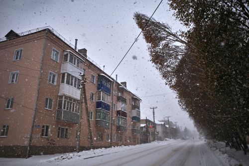Free Snow-covered street in a small town showcasing residential buildings amidst snowfall. Stock Photo