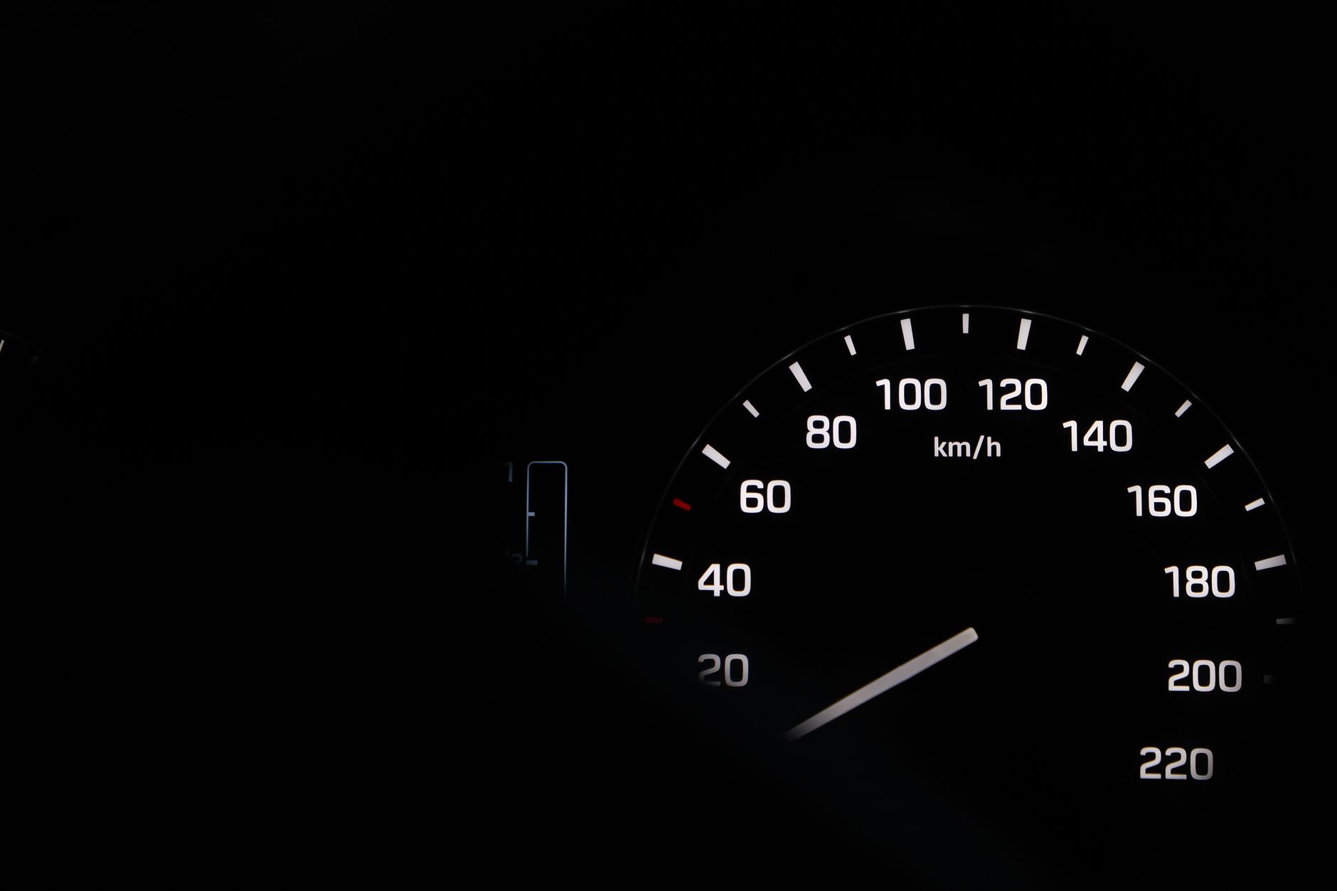 A close-up view of a car speedometer at night with illuminated numbers in black and white.