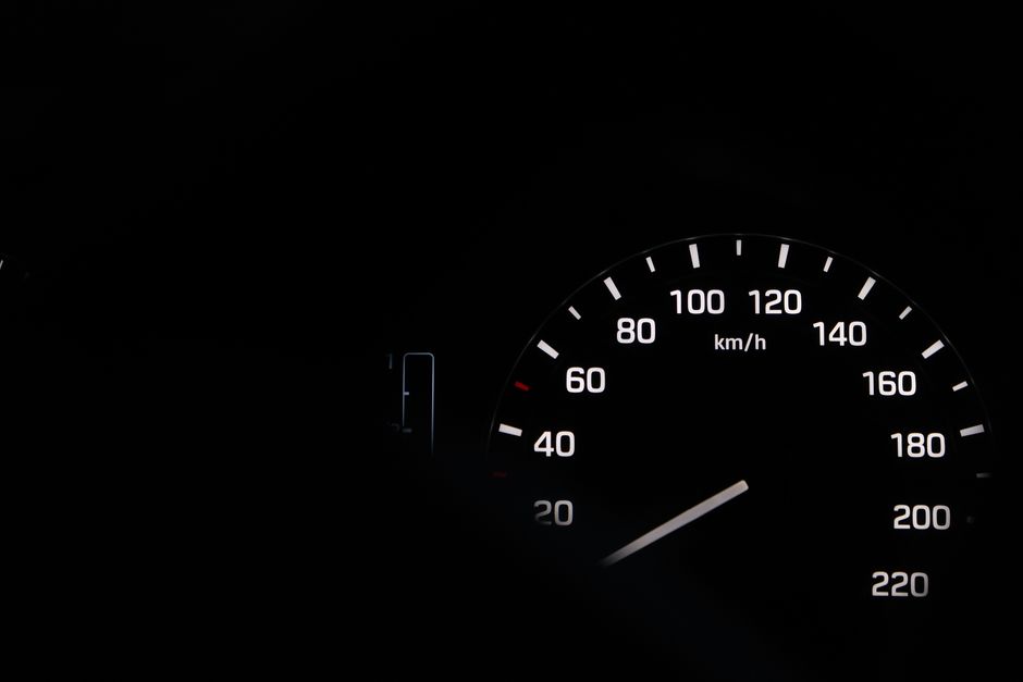 A close-up view of a car speedometer at night with illuminated numbers in black and white.