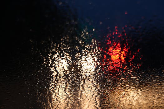 Close-up of rain droplets on a window with blurred city lights, creating an abstract effect.
