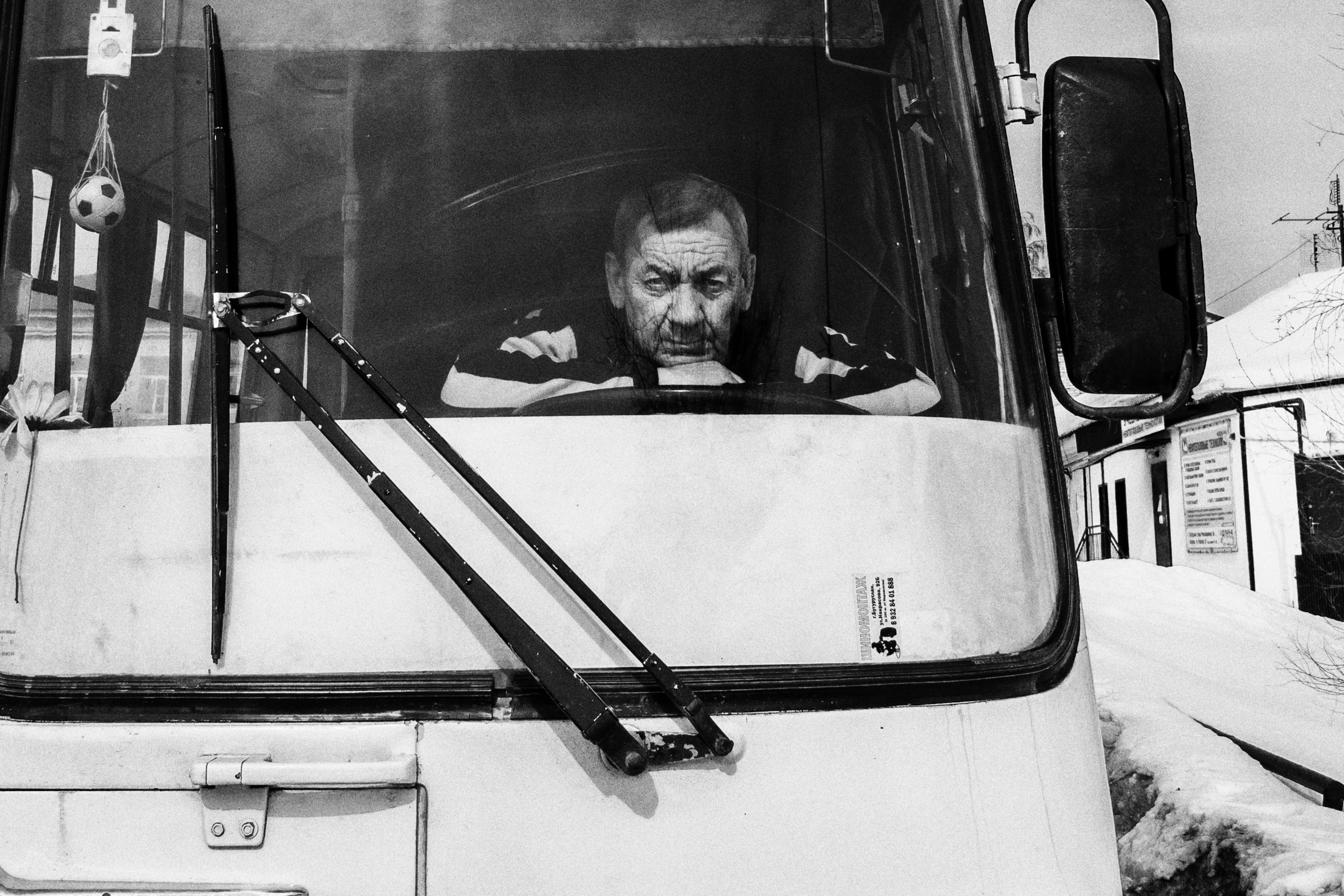 Black and white photo of a bus driver waiting in winter, displaying thoughtful expression.