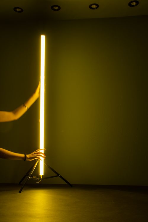 Free Hands adjusting tall, vibrant fluorescent light in dim room, creating a modern atmosphere. Stock Photo