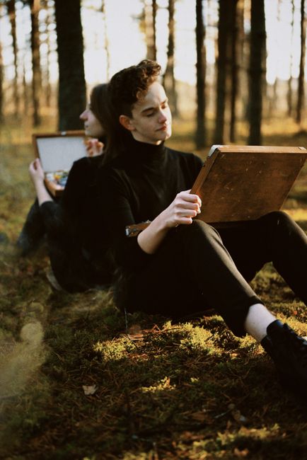 Two people sketching in a sunlit forest, creating art in nature's tranquility.