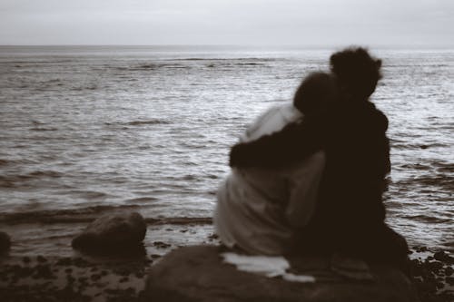 Man with Arms around a Woman Sitting and Looking at the Sea 