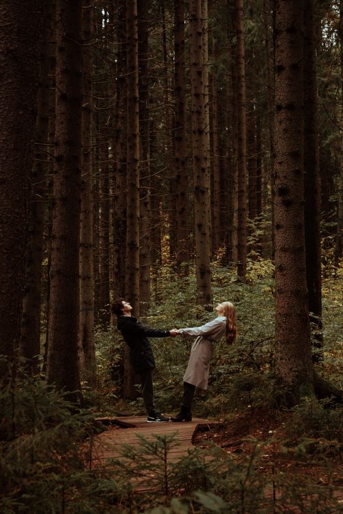 Free A couple holds hands amidst tall trees in an enchanting forest setting. Stock Photo