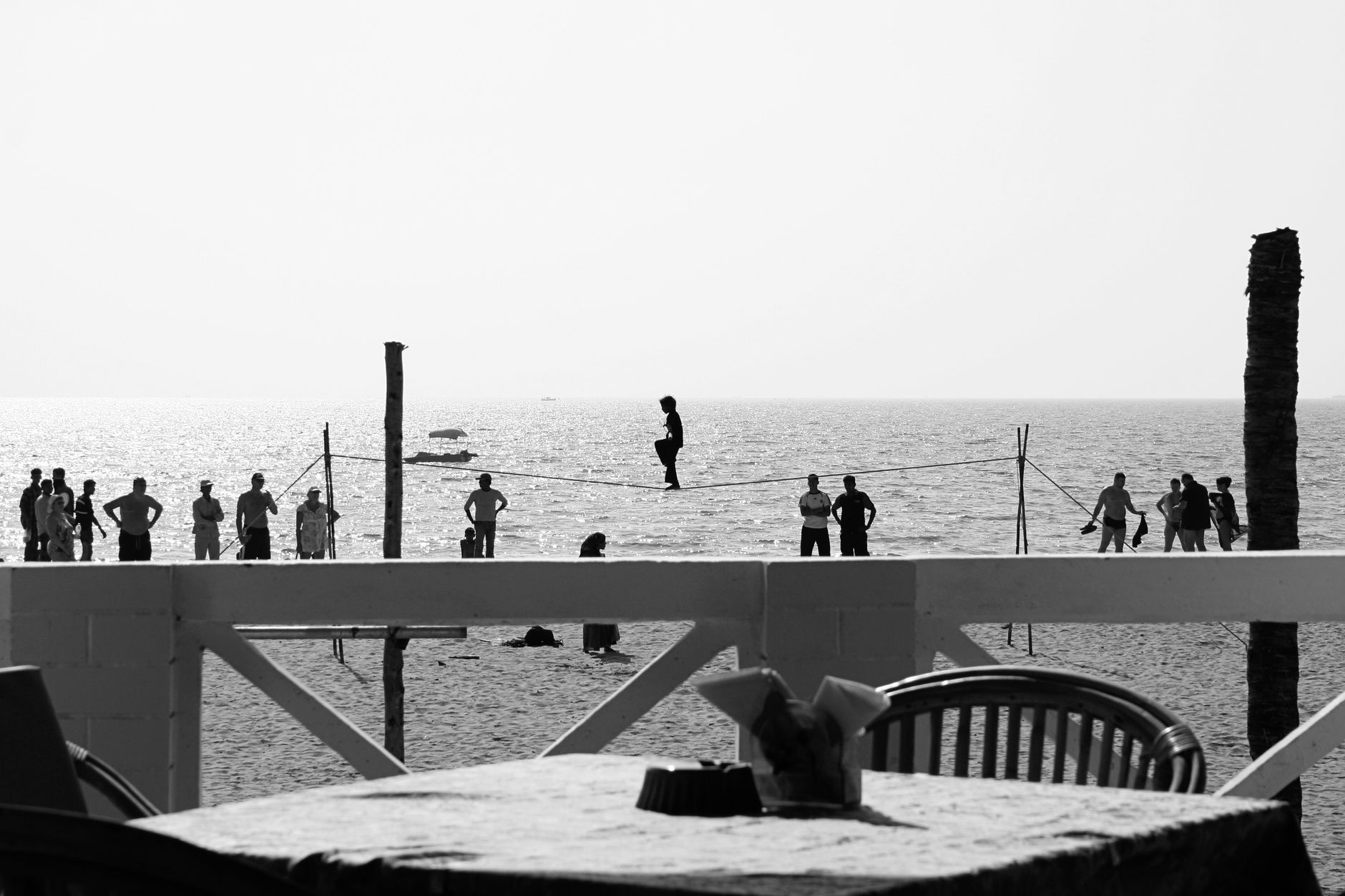 Monochrome image of a beach scene with a tightrope walker and onlookers by the sea.