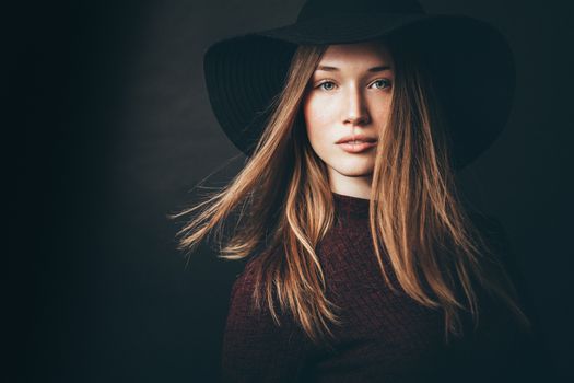 Stylish portrait of a woman with blond hair in a black hat, dramatic lighting.
