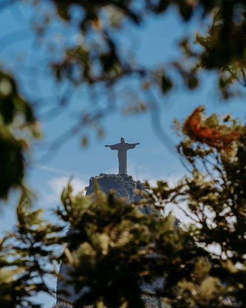Free Christ the Redeemer statue seen through dense foliage in Rio, symbolizing religion and peace. Stock Photo