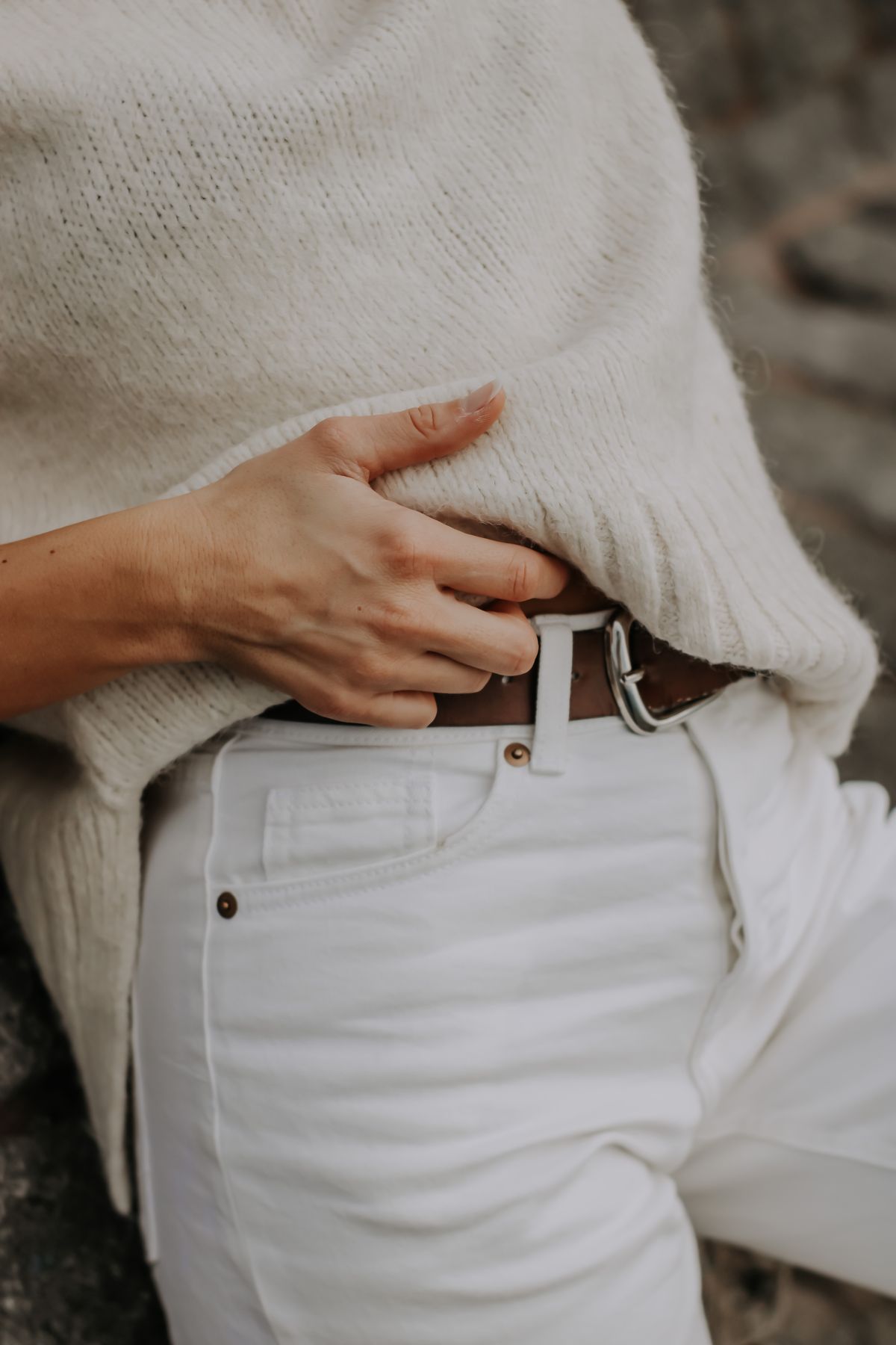 Close-up of a woman styling a belt with light trousers and a cozy knit