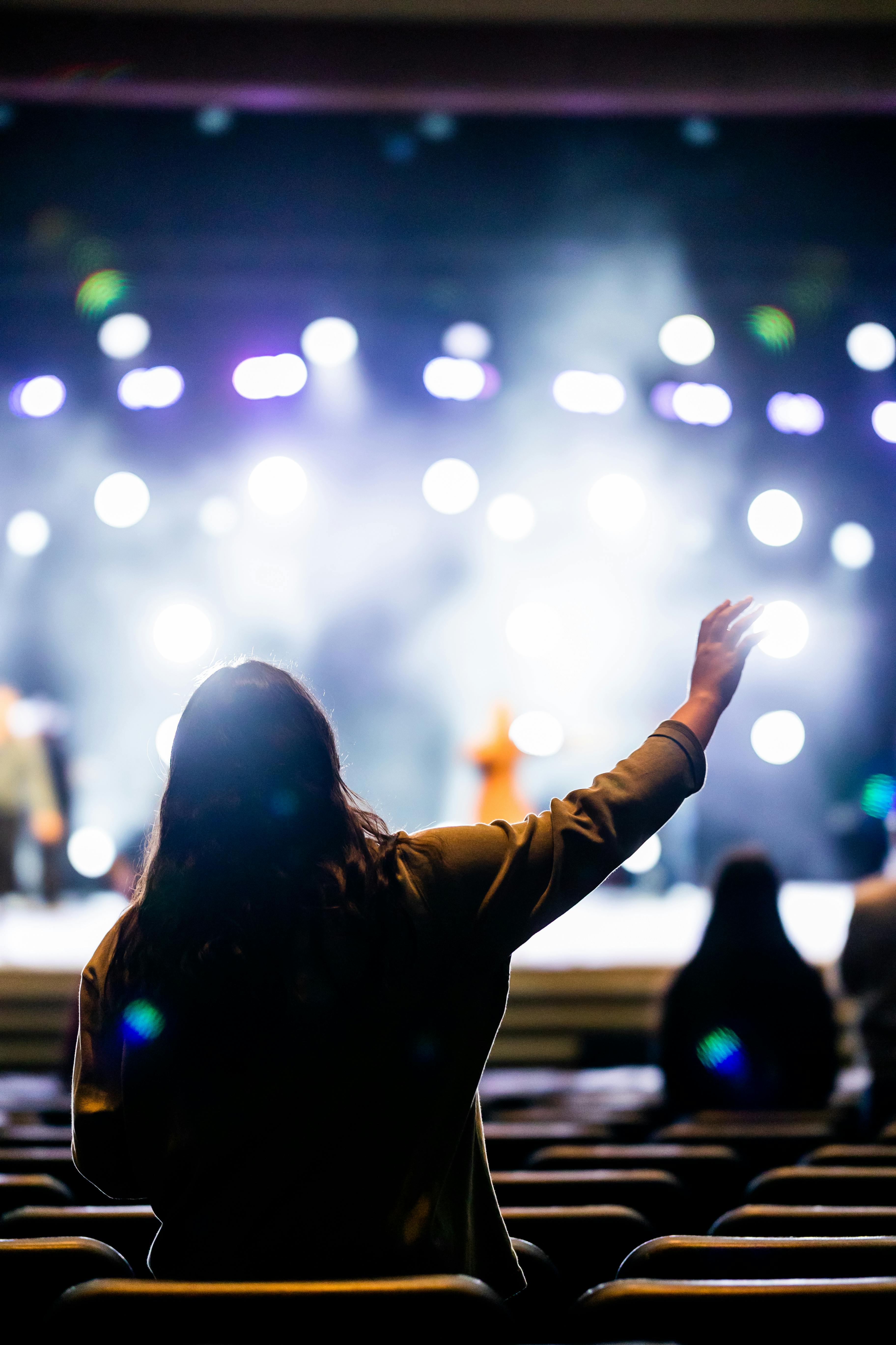 Free Silhouetted audience member raising hand during a vibrant live concert with colorful stage lights. Stock Photo