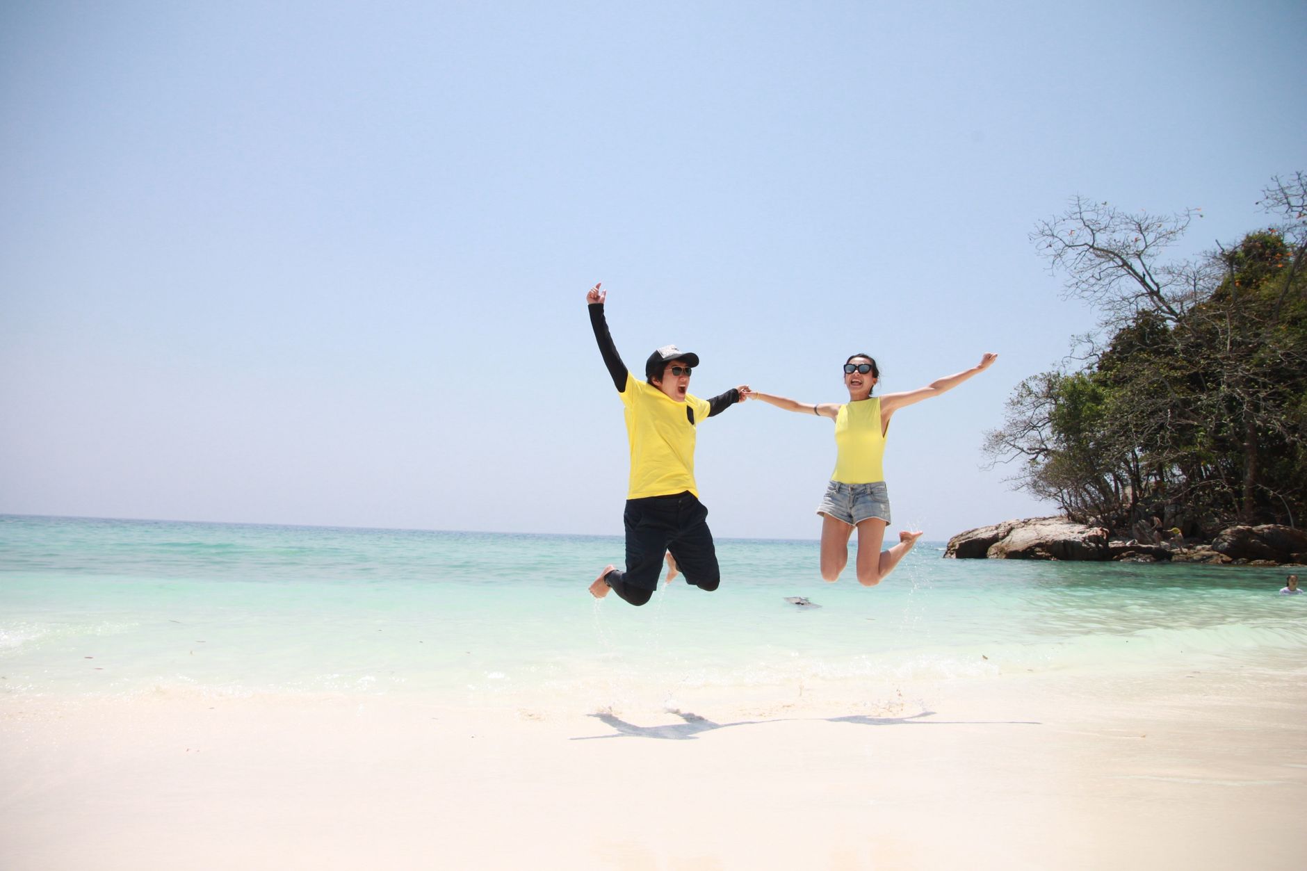 A happy couple jumping on a sunny tropical beach. Ideal for vacation and getaway themes.