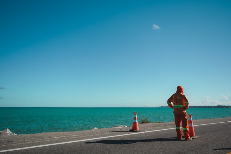 A Worker Wearing An Orange Coverall On A Road By The Sea