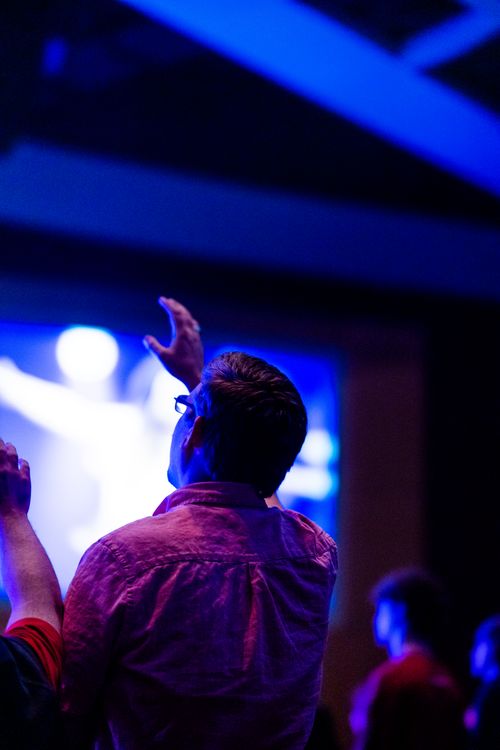 Free Man raising hand at indoor concert with vibrant blue lighting. Perfect for nightlife and music themes. Stock Photo