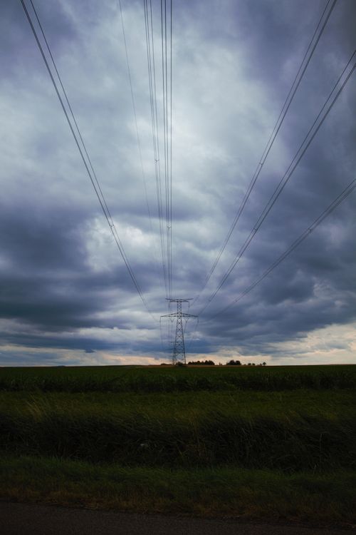 Free Dramatic overcast sky with power lines stretching across a vast green field. Stock Photo
