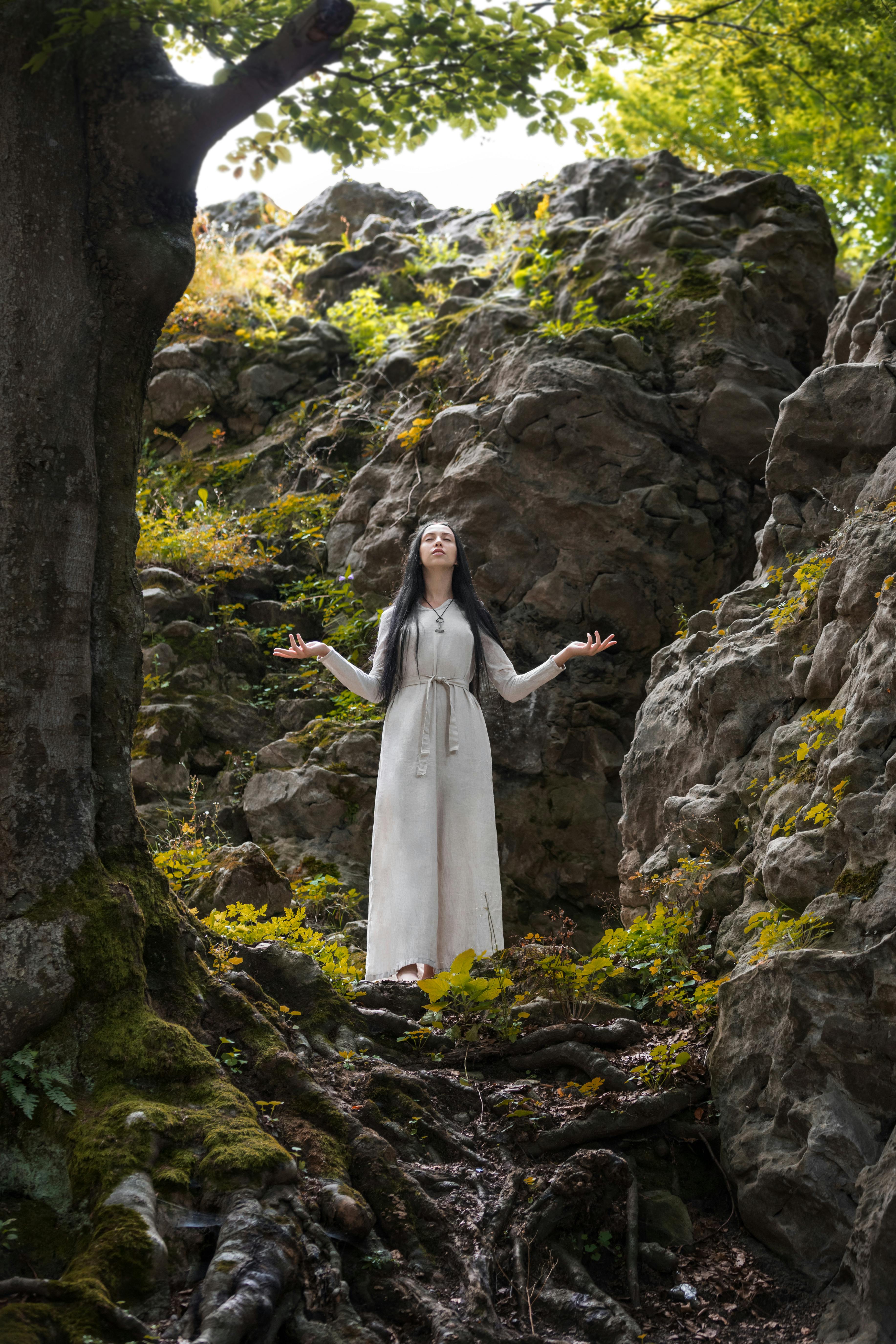 a woman in long dress meditating near big rocks