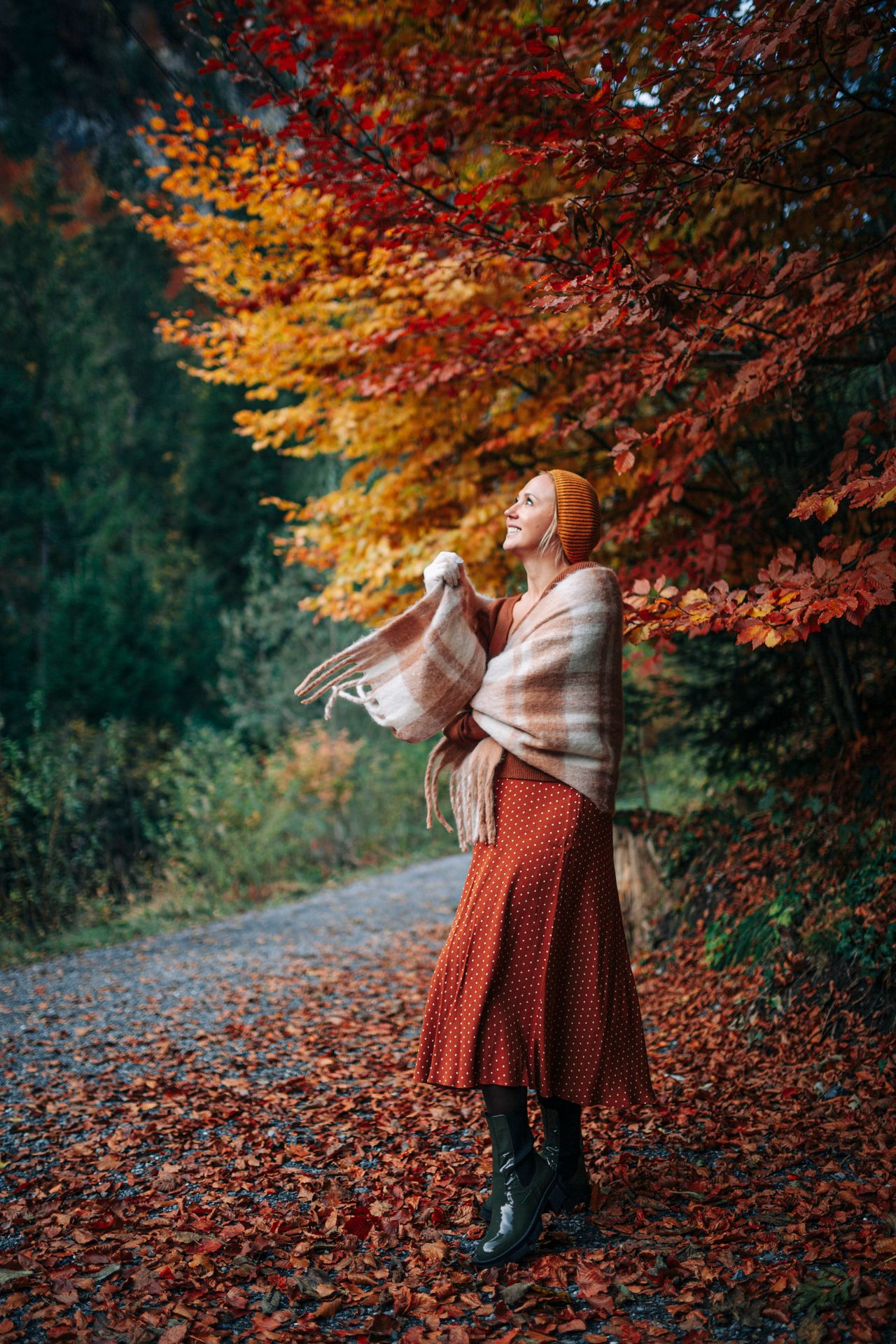 Woman in a rust polka-dot midi skirt and plaid shawl on an autumn path