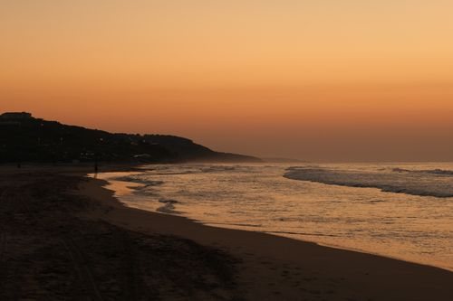 Free Serene beach scene at sunset with gentle waves and a warm sky glow. Stock Photo