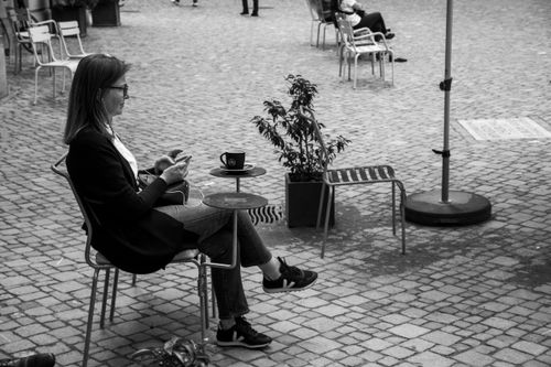 Free Black and white photo of a woman listening to music at an outdoor café. Stock Photo