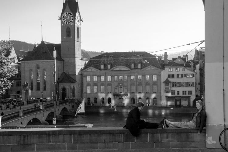 Man And Woman Sitting On Fence In Town