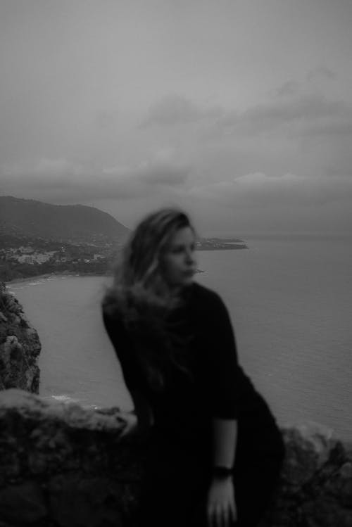 
A Grayscale of a Woman Leaning on a Rock with a Beautiful View