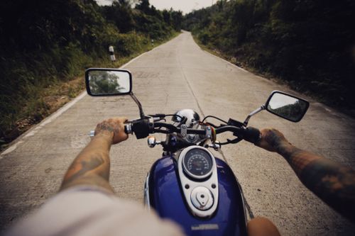 Free A tattooed motorcyclist rides down a scenic rural road, offering a sense of adventure. Stock Photo
