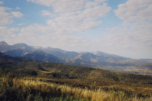 Free Breathtaking view of rolling hills and majestic mountains beneath a cloudy sky, ideal for nature lovers. Stock Photo