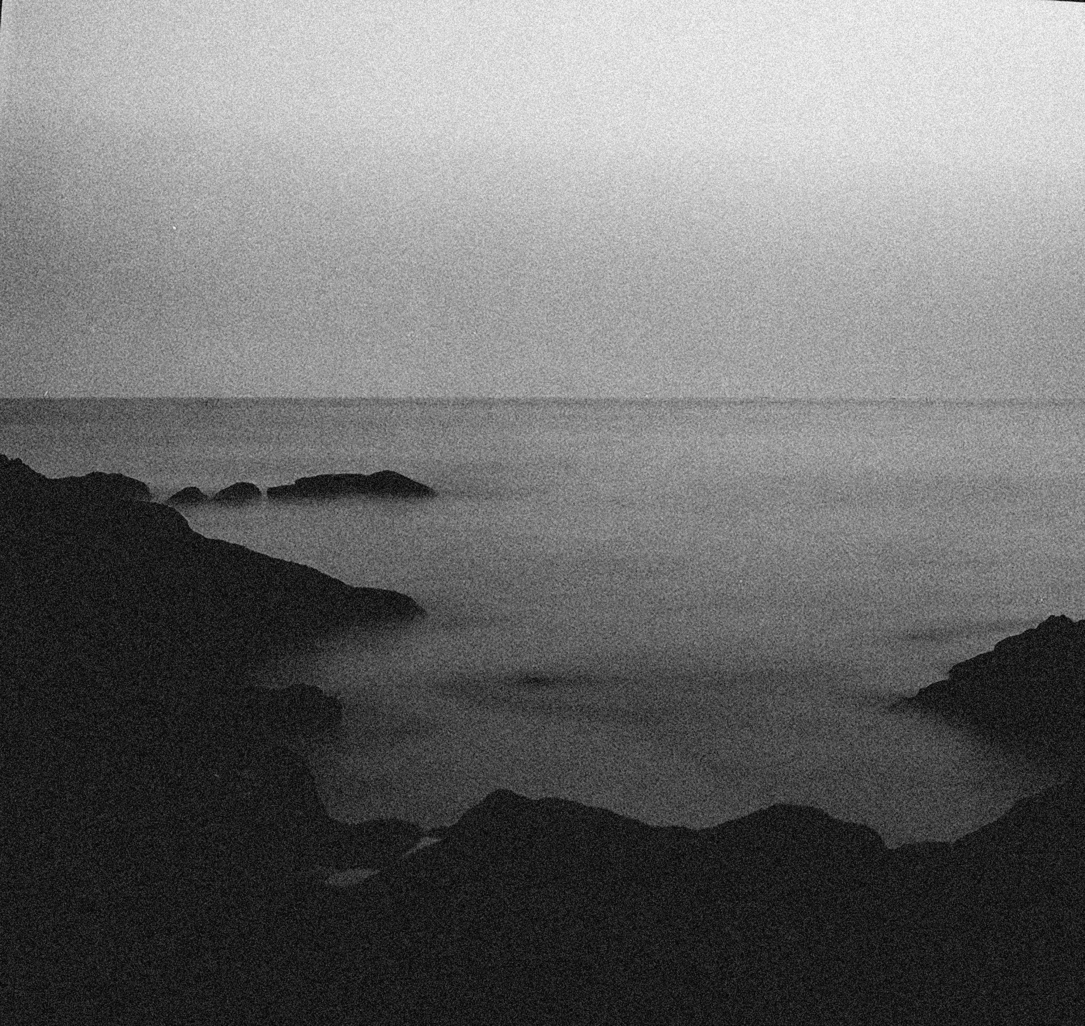 Dramatic black and white photography of a foggy coastal landscape with rocks.