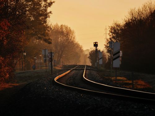 Free A tranquil railway scene captured at sunset with warm golden hues and silhouetted trees. Stock Photo