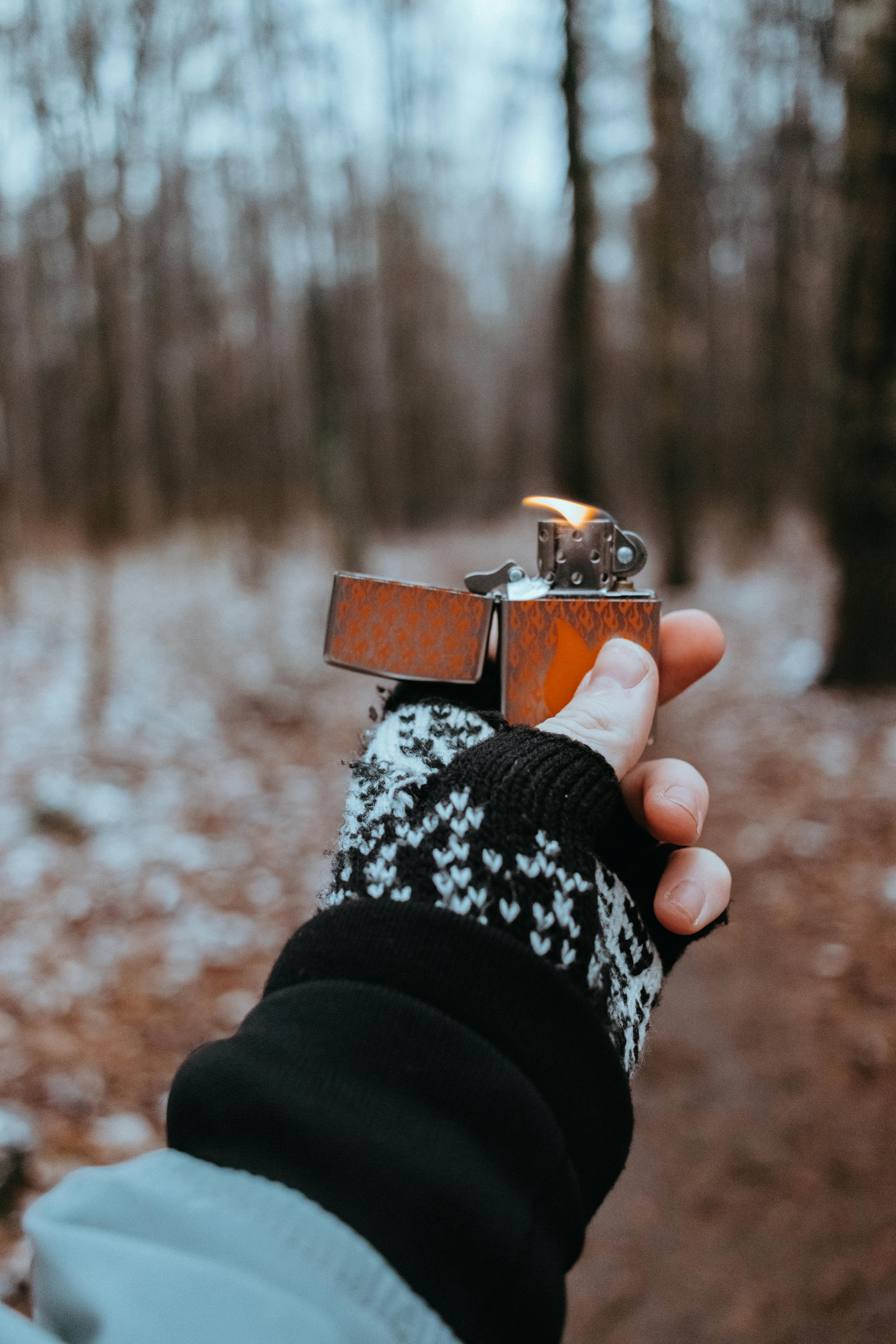 Close-up of a hand in gloves holding a lighter in a forest during fall.