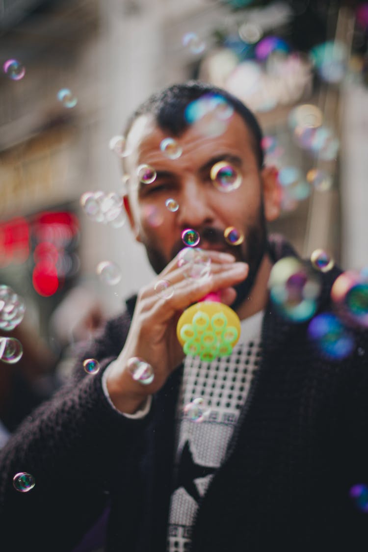 A Man In Black Long Sleeve Shirt Blowing Bubbles From A Toy