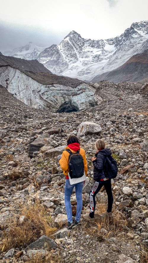 Free Two hikers with backpacks traverse rocky terrain towards majestic snow-capped mountains. Stock Photo