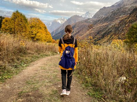 A solitary woman with a backpack hiking through vibrant autumn mountain scenery.
