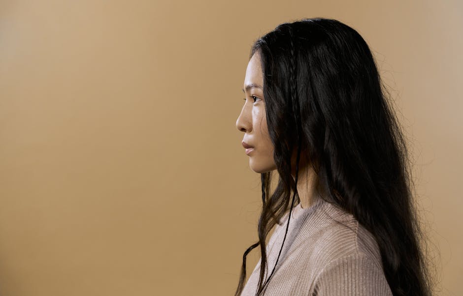 A side profile portrait of a woman in a sweater against a neutral beige background.